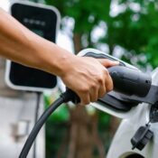 Hand inserting EV charging plug to electric vehicle in focus shot with blurred background of outdoor natural greenery.